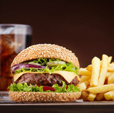 fresh cheeseburger with glass of cola and pile of french fries on wooden table